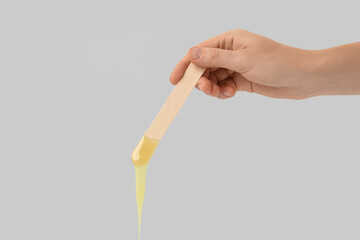 Woman holding spatula with hot depilatory wax on light  background, closeup