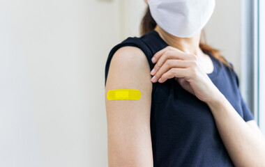 Asian woman wear face mask using adhesive bandage with yellow at arm after injection vaccine. Covid 19 vaccine disease preparing.