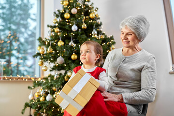 Obraz na płótnie Canvas christmas, holidays and family concept - happy grandmother and baby granddaughter with gift box at home