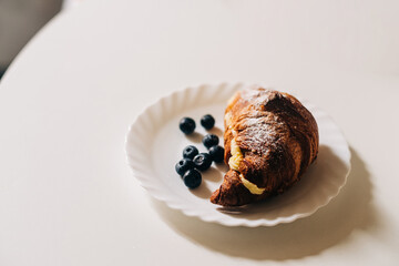 Croissant with cream and blueberry on a white plate, european breakfast concept