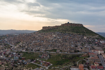 Obraz premium トルコ 丘から見える山の斜面に広がるマルディンの旧市街の街並みと山頂に立つマルディン城と夕焼け空
