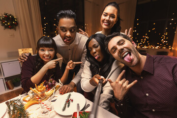 holidays, friendship and celebration concept - multiethnic group of happy friends having christmas dinner at home and taking selfie