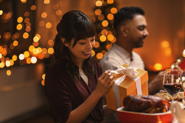 holidays, party and celebration concept - happy smiling woman opening gift box on christmas dinner at home