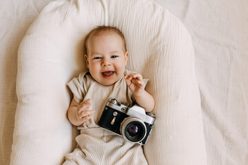 Baby photographer lying in a baby nest, holding a vintage film camera, smiling.