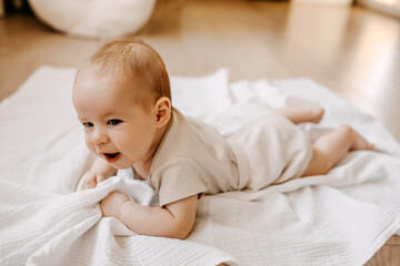 Baby lying on tummy on a white muslin blanket on the floor, smiling.