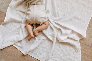 Closeup of barefoot baby lying on tummy on a white muslin blanket on the floor. - obrazy, fototapety, plakaty