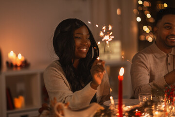 holidays and celebration concept - multiethnic group of happy friends with sparklers having christmas dinner at home