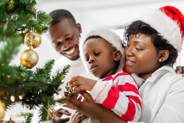 family, winter holidays and people concept - happy african american mother, father and baby son decorating christmas tree at home on