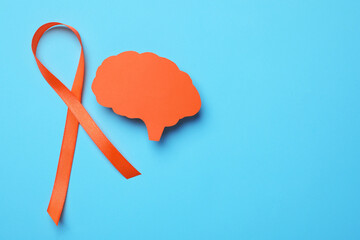 Orange ribbon and paper brain cutout on light blue background, flat lay with space for text....