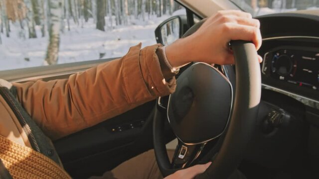 Close up shot of hands of unrecognizable man in warm parka driving car in forest area in winter