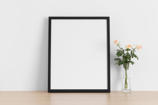 Black frame mockup with a bouquet of a pink roses on the wooden table.