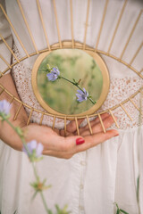 Woman in white wedding dress holding mirror reflecting wild flowers, closeup