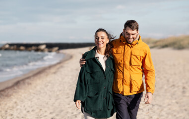 love, relationship and people concept - happy couple walking along autumn beach