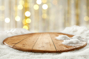 Wooden table with fresh snow and a vacant seat, against a blurry golden background 