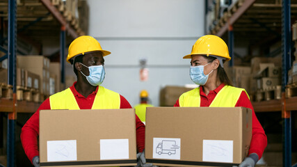 Warehouse workers loading delivery boxes while wearing face mask during corona virus pandemic - Logistic and industry concept