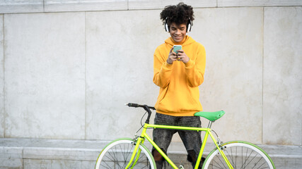 Happy African man using mobile smartphone outdoor while riding with bike in the city - Youth...