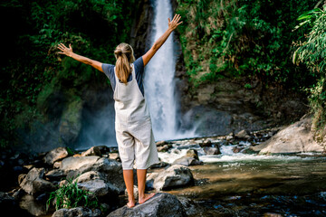 Woman raising her hands as a freedom gesture facing a waterfall in the forest