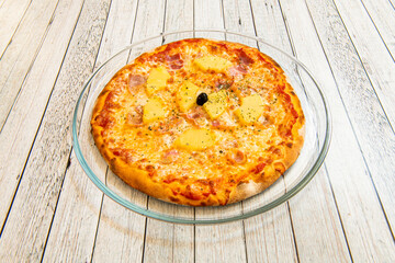 Tropical Hawaiian Pizza with Pineapple Chunks with Black Olive, Oregano, Smoked Bacon and Mozzarella Cheese on Glass Tray