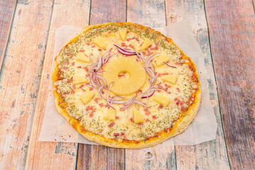 Tropical pizza with a slice of pineapple and slices around it with red onion, pieces of smoked bacon and mozzarella cheese with lots of oregano