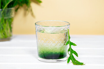 Green Chlorophyll or Chlorella drink in glass with water on white table, Orange Background. Green Drops in clear water, Antioxidant food and drinks.