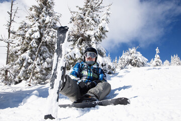 man of about 35-40 years old in winter clothes on skis sits in the snow on a sunny winter day....