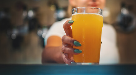 woman hand hold glass of light beer stands on a table in a bar or pub