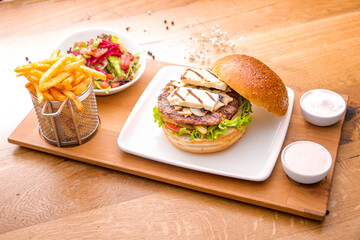 Close up view of Fresh tasty beef burger and french fries on wooden tray with seasoning on rustic table