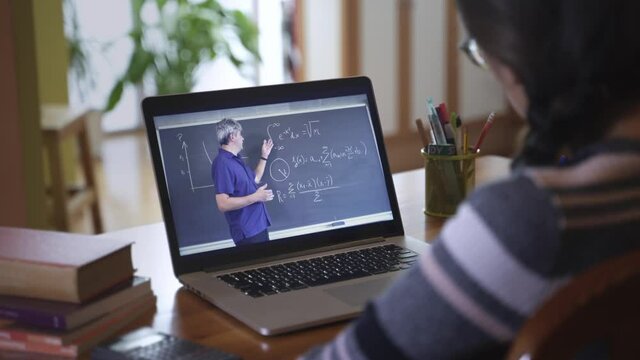 Female Student taking notes while watching video lecture with Math Professor from home. Learning College or High School courses with Online Education University 
