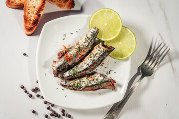 Appetizer of sardines in oil with parsley and paprika on a plate with some toast and lemon slices.