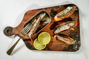 Arrangement of Spanish tapas of sardines in olive oil on toasts on a rustic wooden board and a can...