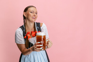 Adorable Oktoberfest woman, waitress wearing a traditional Bavarian or german dirndl holding one liter beer glass isolated on pink studio background.