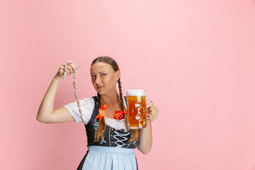 Adorable Oktoberfest woman, waitress wearing a traditional Bavarian or german dirndl holding one liter beer glass isolated on pink studio background.