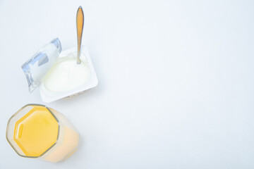 A cup of natural yogurt, a dessert spoon and a glass of orange juice on a white background.