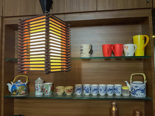 Colorful bone china ans ceramic cups and mugs with designs on them displayed neatly in a wooden  shelf