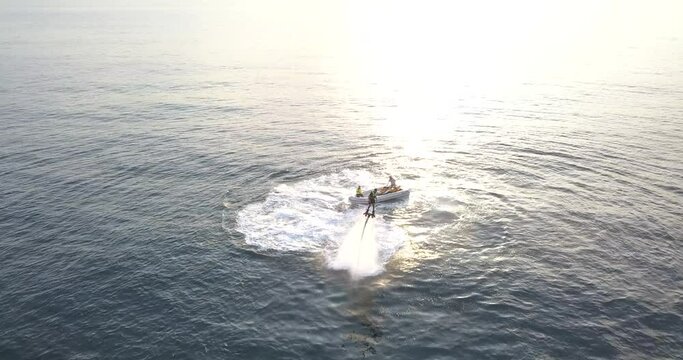 high aerial around person using water jetpack with sunset in background
