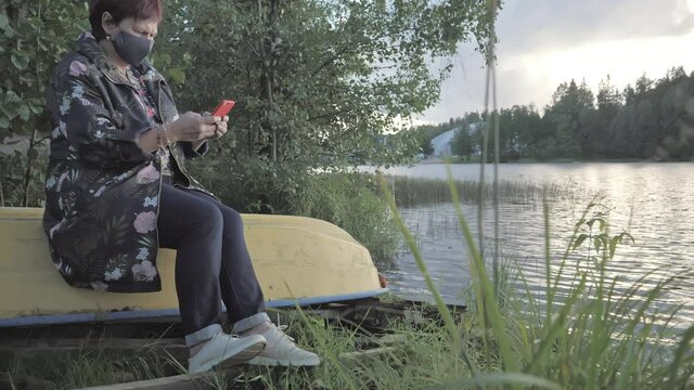 The middle aged lady texting on her phone in Espoo Finland taking a break and rest on the boat beside the lake on a sunset.4k