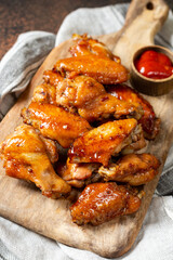 Homemade baked or fried chicken wings in barbecue sauce on a serving board on a cooking table closeup	