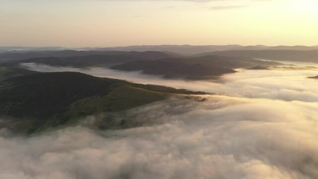 Drone flyght over flowing morning fog in summer mountains. Beautiful sunrise light glowing on forest, medows and green hills. UHD 4k video