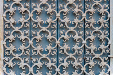 Window metal lattice with vintage patterns on the background of closed blue wooden shutters