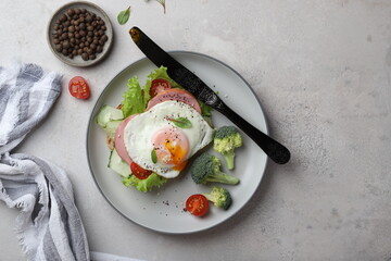 beautiful healthy food healthy breakfast sandwich with poached egg, lettuce, broccoli and cherry tomatoes on a plate on a gray background under concrete top view, with a knife and a napkin modern styl