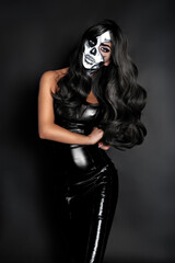 Female model in Halloween silence. Sexy brunette woman in skull makeup and latex costume on black...