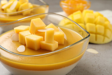 Delicious panna cotta with mango coulis and fresh fruit pieces on grey table, closeup