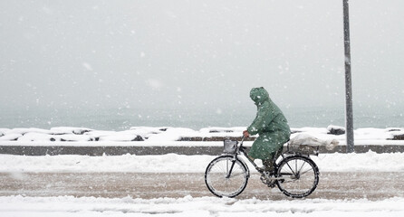 Man rides a bicycle in a snowfall in a sea side road