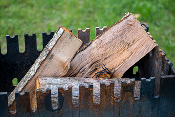 Chopped wood in a black fireplace. Picnic tools for outdoor camping. Natural raw firewood ready to be set on fire. Selective focus on the texture of the material, blurred background.