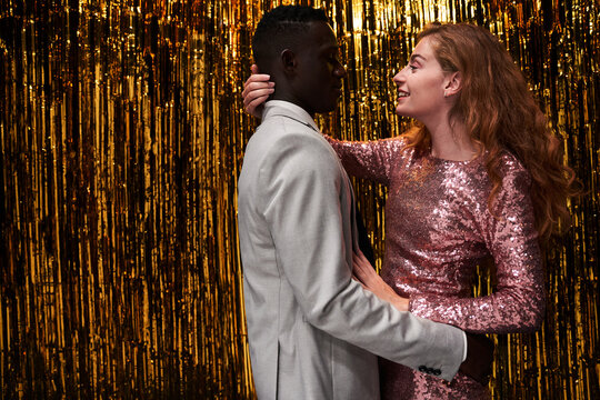 Loving diverse couple embracing against tinsel during festive event