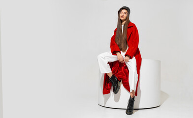 Fashion studio photo of stylish european brunette woman in red coat and black hat posing on white...