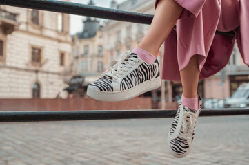 Trendy fashion details: woman wearing stylish sneakers with zebra print, posing in street of European city. Copy, empty space for text - 457551890