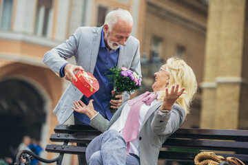 Beautiful senior couple dating outdoors. Man giving his wife present and flowers.
