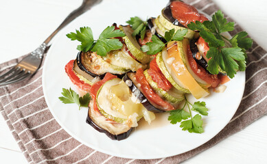 baked vegetables with cheese and parsley on a white plate, home dinner idea. vegetarian menu. sliced and roasted eggplants, tomatoes and zucchini.