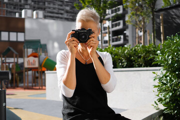 A beautiful senior woman sits in a park and takes photos with a photo camera.